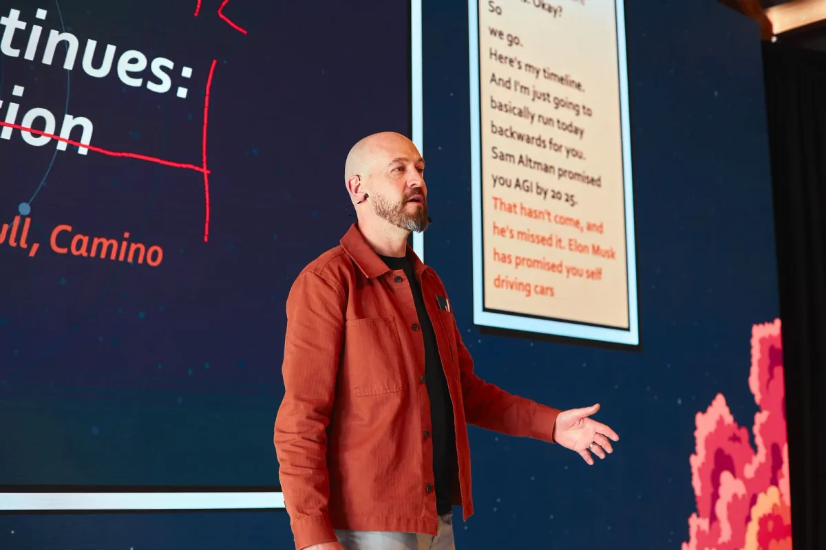 James Turnbull speaking on stage in a rust-coloured jacket
